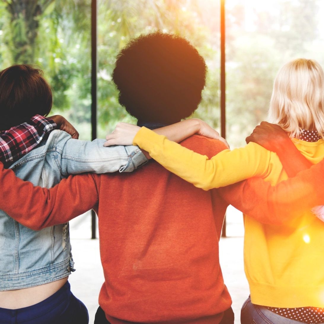 Three friends with arms around each other facing a sunny window